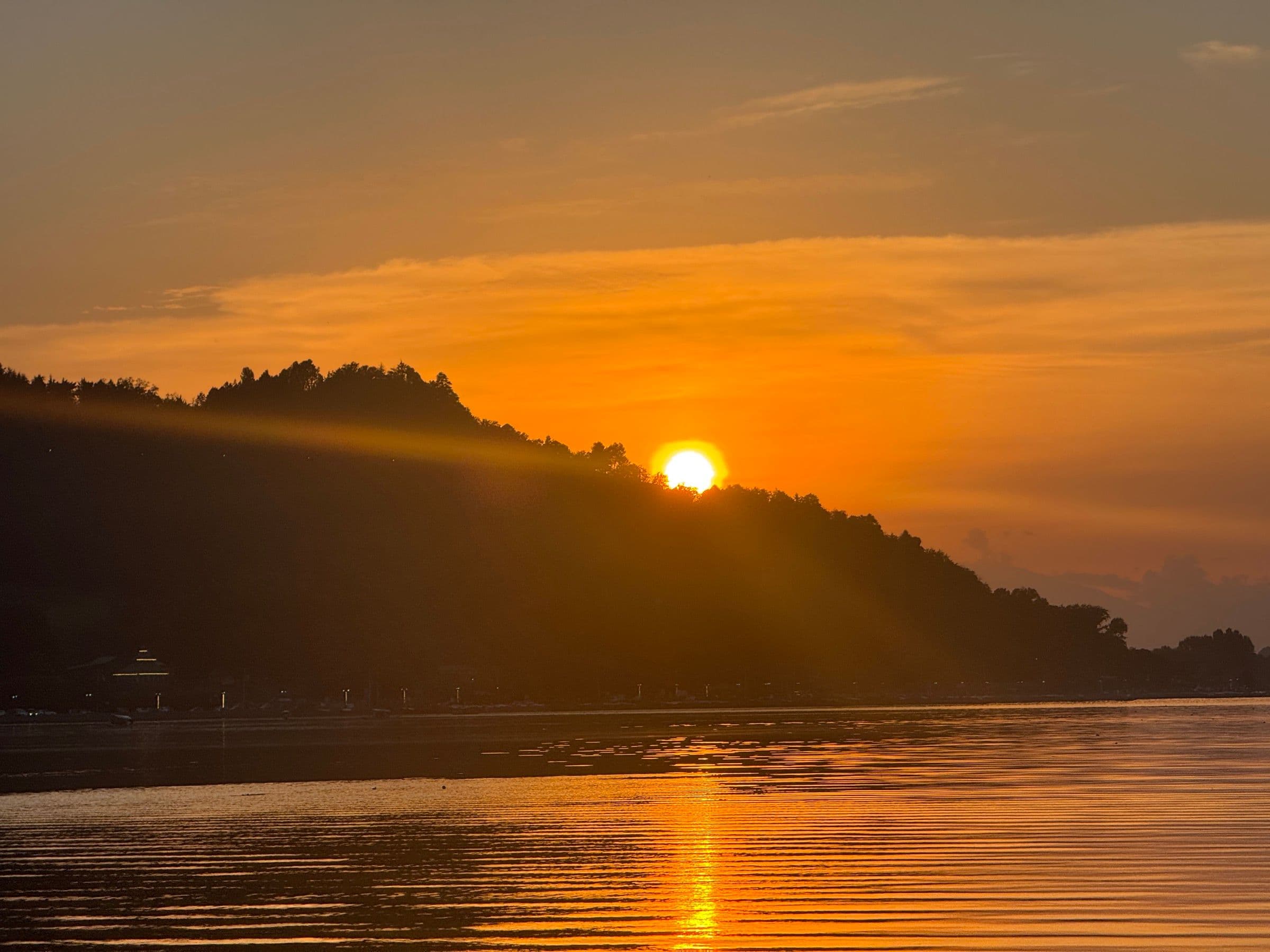 Sunset over the water in Kashmir, hills silhouetted against an orange sky