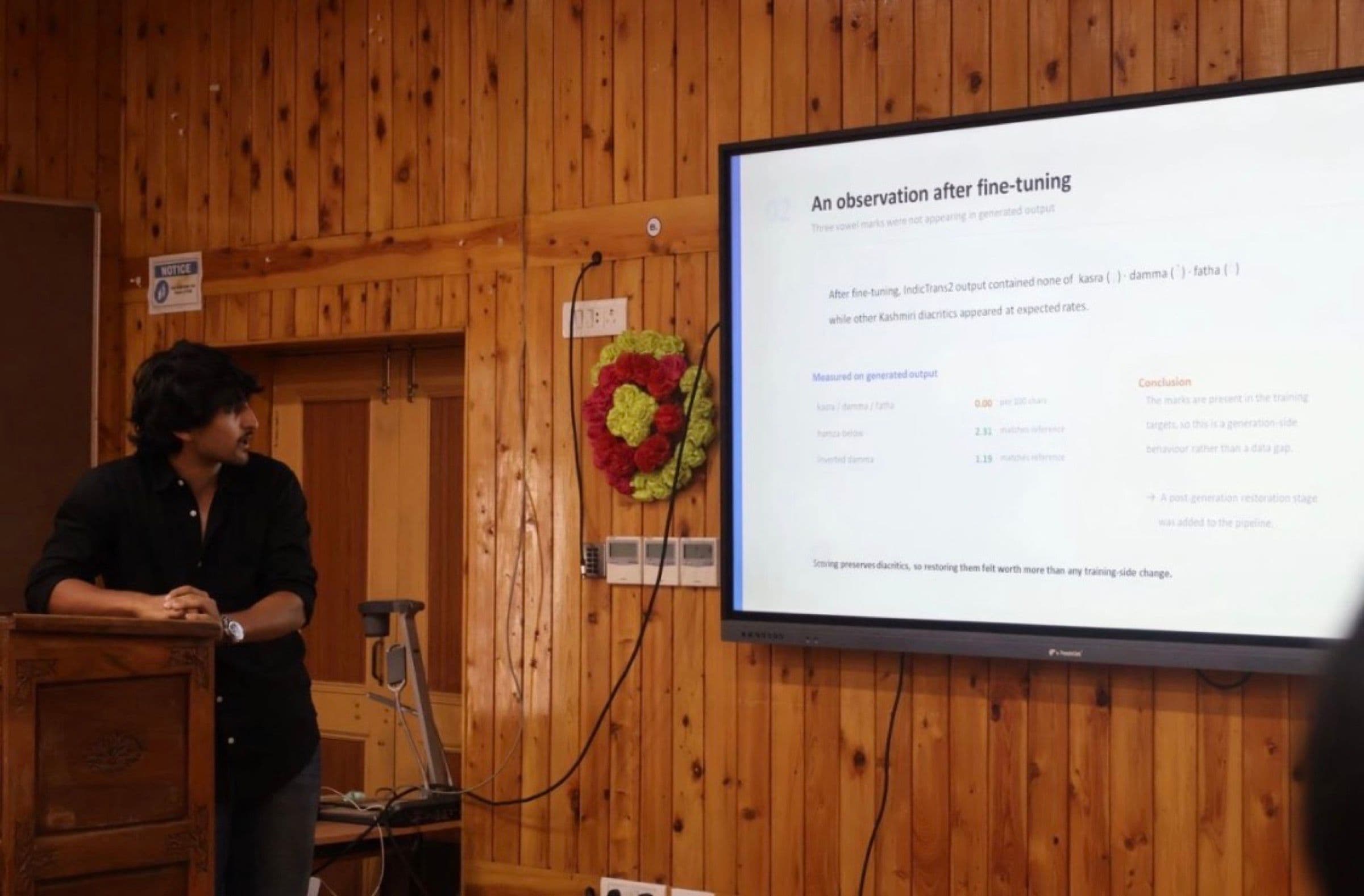 Azhad presenting at KATHE 2026, beside a slide reading 'An observation after fine-tuning: three vowel marks were not appearing in generated output'